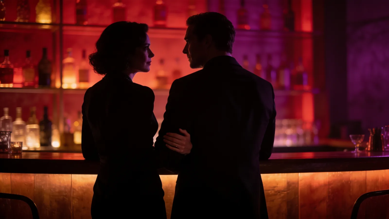 Een vrouw en een man in het zwart in gesprek aan een bar met verlichte flessen, haar hand op zijn arm
